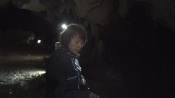 Movie still from “Cave of Forgotten Dreams” (2010), directed by Werner Herzog – A woman is standing in a cave at night with a flashlight; Medium shot, Low angle