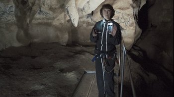 Movie still from “Cave of Forgotten Dreams” (2010), directed by Werner Herzog – A man standing inside of a cave holding a cell phone; Wide shot, High angle