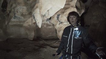 Movie still from “Cave of Forgotten Dreams” (2010), directed by Werner Herzog – A woman standing in front of a cave with paintings; Medium shot, High angle