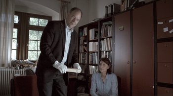 Movie still from “Cave of Forgotten Dreams” (2010), directed by Werner Herzog – A man and a woman are in a room with books; Medium shot, Over the shoulder angle