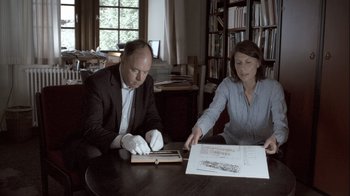 Movie still from “Cave of Forgotten Dreams” (2010), directed by Werner Herzog – A man and a woman sitting at a table looking at a book; Medium shot, High angle