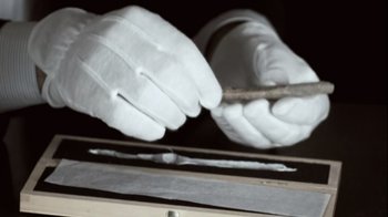Movie still from “Cave of Forgotten Dreams” (2010), directed by Werner Herzog – A pair of hands wearing white gloves holding a piece of metal; Extreme Close Up shot, High angle