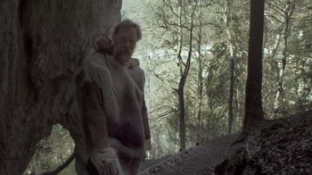 Movie still from “Cave of Forgotten Dreams” (2010), directed by Werner Herzog – A man in a fur coat standing next to a tree; Medium shot, Low angle