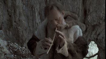Movie still from “Cave of Forgotten Dreams” (2010), directed by Werner Herzog – An old man in a fur coat is playing a flute; Close Up shot, Low angle