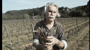 Movie still from “Cave of Forgotten Dreams” (2010), directed by Werner Herzog – An older man holding a bunch of sticks in his hands; Medium shot, Low angle