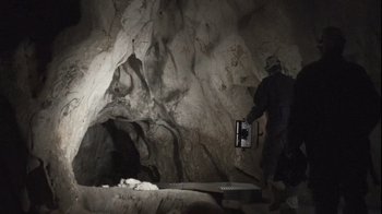 Movie still from “Cave of Forgotten Dreams” (2010), directed by Werner Herzog – A person in a cave holding a metal object; Wide shot, Low angle
