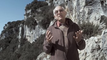 Movie still from “Cave of Forgotten Dreams” (2010), directed by Werner Herzog – An older man standing in front of a cliff; Medium shot, Low angle