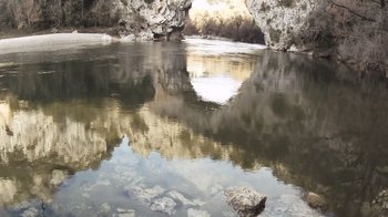 Movie still from “Cave of Forgotten Dreams” (2010), directed by Werner Herzog – A body of water surrounded by rocks and trees; Extreme Wide shot, High angle