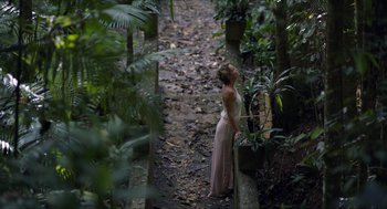 A woman in a pink dress standing on a path in the woods