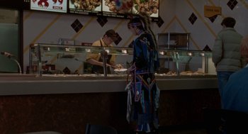 Movie still from “Certain Women” (2016), directed by Kelly Reichardt – A man in native american garb standing in front of a counter; Wide shot, Over the shoulder angle