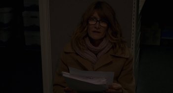 Movie still from “Certain Women” (2016), directed by Kelly Reichardt – A woman holding a stack of papers in a dark room; Medium shot, Over the shoulder angle