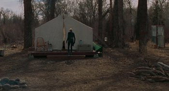 Movie still from “Certain Women” (2016), directed by Kelly Reichardt – A man standing in front of a tent in the woods; Wide shot, High angle