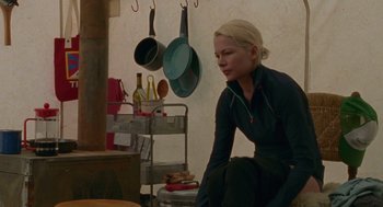 Movie still from “Certain Women” (2016), directed by Kelly Reichardt – A woman sitting on a stool in front of some pans hanging on the wall; Medium shot, Over the shoulder angle