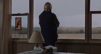 Movie still from “Certain Women” (2016), directed by Kelly Reichardt – A woman standing in front of a window looking out at a field; Medium shot, Over the shoulder angle
