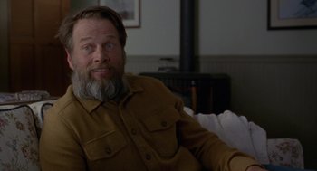 Movie still from “Certain Women” (2016), directed by Kelly Reichardt – A man sitting on a couch in a living room; Close Up shot, Over the shoulder angle