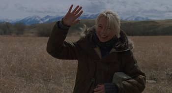 Movie still from “Certain Women” (2016), directed by Kelly Reichardt – A woman in a field waving at the camera; Medium shot, Over the shoulder angle