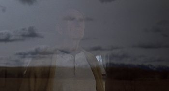 Movie still from “Certain Women” (2016), directed by Kelly Reichardt – A man standing in front of a window with clouds in the background; Medium shot, Low angle
