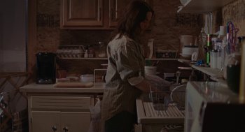 Movie still from “Certain Women” (2016), directed by Kelly Reichardt – A woman standing in a kitchen washing dishes; Medium shot, High angle