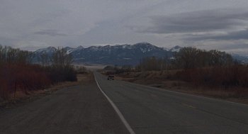 Movie still from “Certain Women” (2016), directed by Kelly Reichardt – A car driving down a road near a mountain range; Extreme Wide shot, High angle
