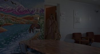 Movie still from “Certain Women” (2016), directed by Kelly Reichardt – A woman standing in front of a table in a room; Wide shot, Over the shoulder angle