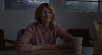 Movie still from “Certain Women” (2016), directed by Kelly Reichardt – A woman sitting at a wooden table with a cup of coffee; Medium shot, Over the shoulder angle