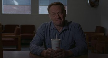 Movie still from “Certain Women” (2016), directed by Kelly Reichardt – A man sitting at a table holding a drink; Close Up shot, Over the shoulder angle