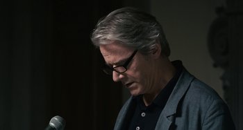 Movie still from “Certified Copy” (2010), directed by Abbas Kiarostami – A man with glasses is looking down at a microphone; Close Up shot, Over the shoulder angle