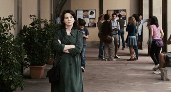 Movie still from “Certified Copy” (2010), directed by Abbas Kiarostami – A woman in a green dress standing in front of a group of people; Medium shot, Over the shoulder angle