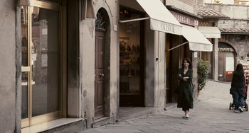 Movie still from “Certified Copy” (2010), directed by Abbas Kiarostami – A woman walking down the street holding an umbrella; Wide shot, Over the shoulder angle
