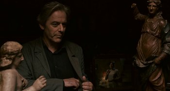 Movie still from “Certified Copy” (2010), directed by Abbas Kiarostami – A man standing in front of a mirror in a dark room; Close Up shot, Over the shoulder angle