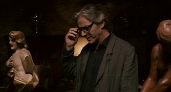 Movie still from “Certified Copy” (2010), directed by Abbas Kiarostami – An older man wearing glasses and a jacket is holding his hand up to his face; Close Up shot, High angle