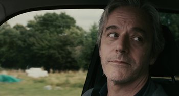 Movie still from “Certified Copy” (2010), directed by Abbas Kiarostami – A person in a car with trees in the background; Close Up shot, Over the shoulder angle