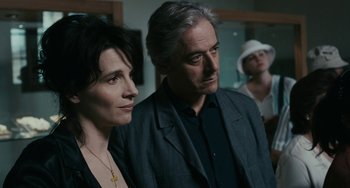 Movie still from “Certified Copy” (2010), directed by Abbas Kiarostami – A man and a woman standing next to each other in a room; Close Up shot, Over the shoulder angle