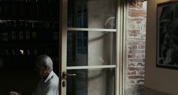 Movie still from “Certified Copy” (2010), directed by Abbas Kiarostami – An older man standing in front of a door; Medium shot, Over the shoulder angle