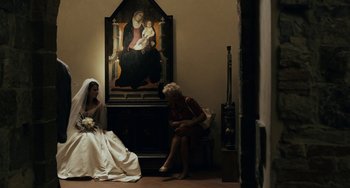 Movie still from “Certified Copy” (2010), directed by Abbas Kiarostami – A woman sitting next to a woman holding a bouquet of flowers; Wide shot, Over the shoulder angle