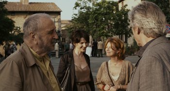 Movie still from “Certified Copy” (2010), directed by Abbas Kiarostami – A group of people standing next to each other on a street; Medium shot, Over the shoulder angle