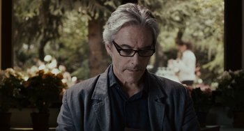 Movie still from “Certified Copy” (2010), directed by Abbas Kiarostami – A person wearing glasses and a jacket; Close Up shot, Over the shoulder angle