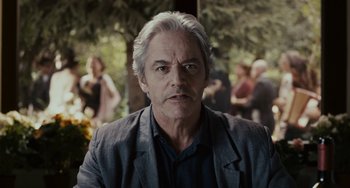 Movie still from “Certified Copy” (2010), directed by Abbas Kiarostami – An older man with white hair is looking at the camera; Close Up shot, Over the shoulder angle