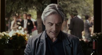 Movie still from “Certified Copy” (2010), directed by Abbas Kiarostami – An older man with grey hair is looking down; Close Up shot, Over the shoulder angle