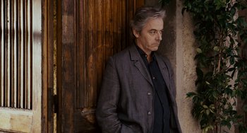Movie still from “Certified Copy” (2010), directed by Abbas Kiarostami – A man standing in front of a wooden wall; Medium shot, Low angle