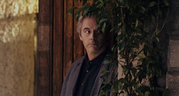 Movie still from “Certified Copy” (2010), directed by Abbas Kiarostami – A man standing in front of a tree looking at the camera; Medium shot, Low angle