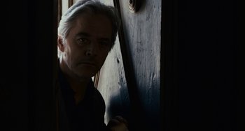 Movie still from “Certified Copy” (2010), directed by Abbas Kiarostami – A man standing in front of a wooden door; Close Up shot, Low angle