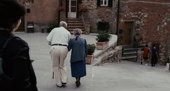 Movie still from “Certified Copy” (2010), directed by Abbas Kiarostami – An older man and woman walking down a street; Wide shot, High angle