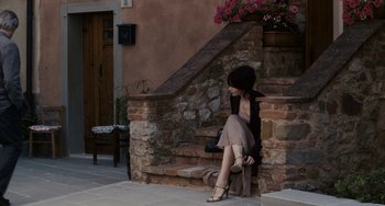 Movie still from “Certified Copy” (2010), directed by Abbas Kiarostami – A woman sitting on a stone wall near a stone staircase; Wide shot, High angle