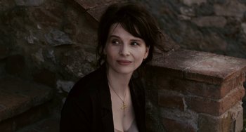 Movie still from “Certified Copy” (2010), directed by Abbas Kiarostami – A woman wearing a black jacket and a cross necklace; Close Up shot, High angle