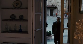 Movie still from “Certified Copy” (2010), directed by Abbas Kiarostami – An older man standing at the entrance of a building; Wide shot, Over the shoulder angle