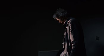Movie still from “Certified Copy” (2010), directed by Abbas Kiarostami – A man standing in the dark with his head turned to the side; Medium shot, Low angle