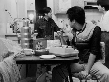 Movie still from “Chan Is Missing” (1982), directed by Wayne Wang – Two men sitting at a table in front of a cake; Medium shot, Over the shoulder angle