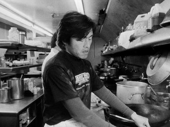 Movie still from “Chan Is Missing” (1982), directed by Wayne Wang – A man sitting in a kitchen preparing food; Medium shot, Low angle