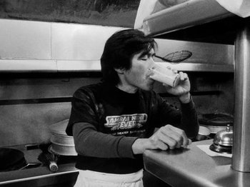 Movie still from “Chan Is Missing” (1982), directed by Wayne Wang – A man in a kitchen drinking from a cup; Medium shot, High angle